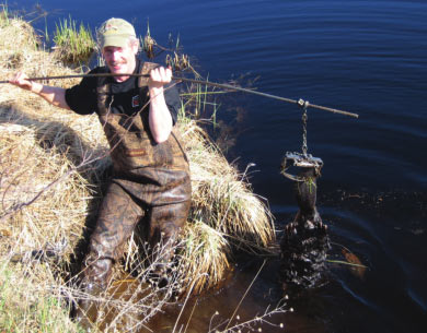 Tim Caven on the bank of a river holding a trap with a beaver caught in it. 