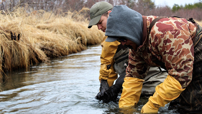 2 men in a river wearing gauntlets trapping animals